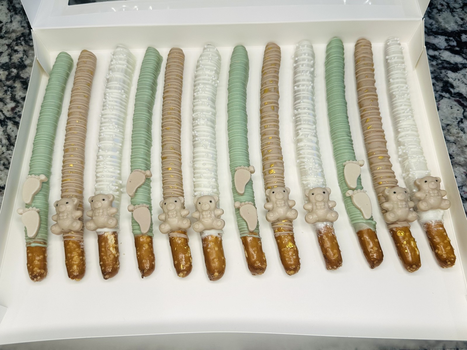 Soft sage, ivory, and gold baby shower chocolate covered pretzels with teddy bear and baby feet details