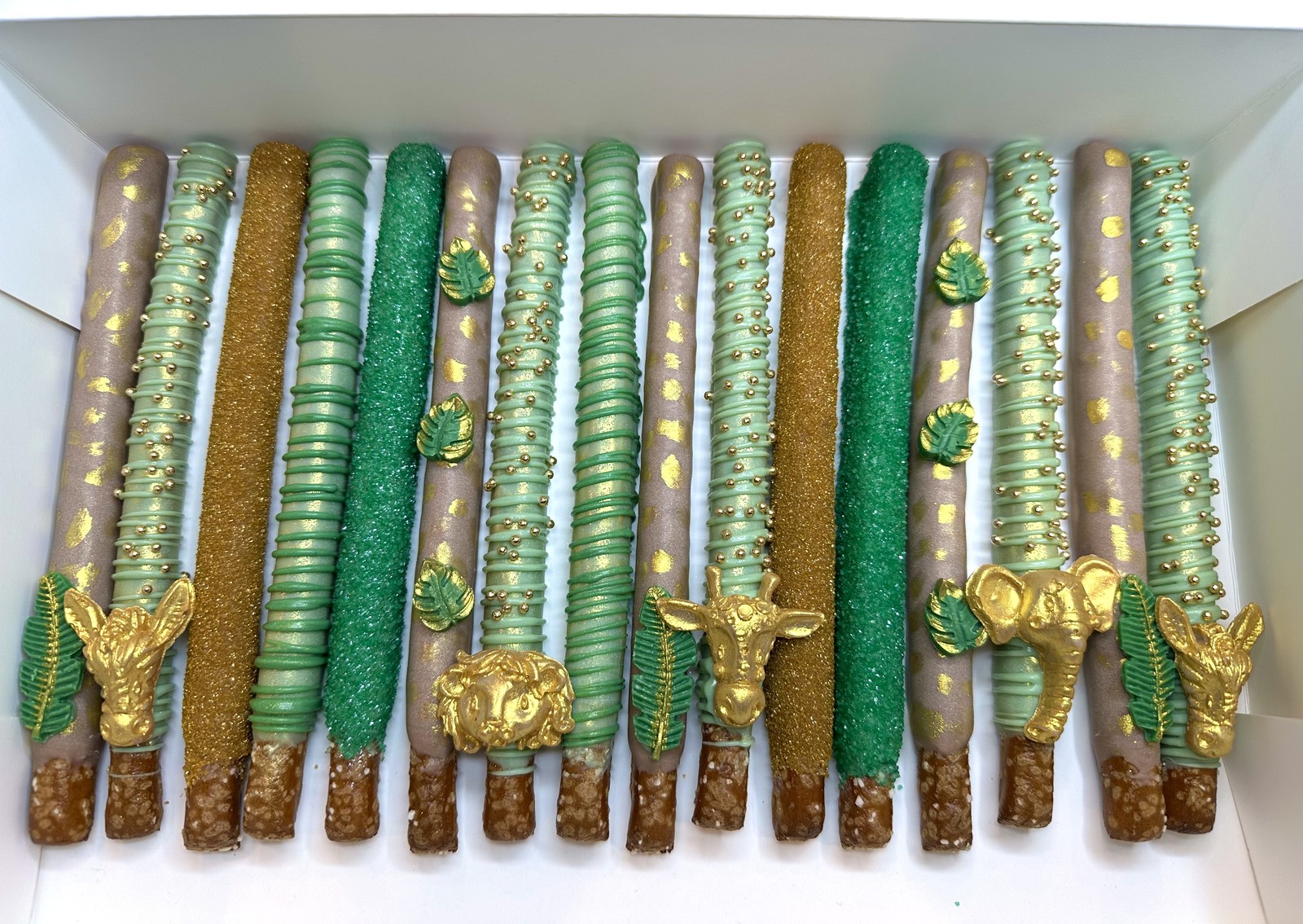 Luxury sage green, emerald, taupe, and gold chocolate covered pretzel rods with jungle animal and tropical leaf details