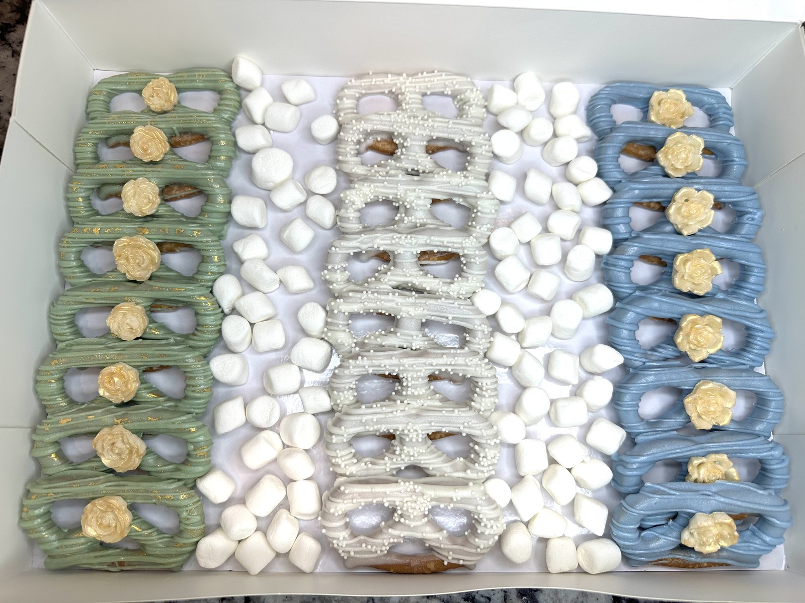 Sage green, ivory, and dusty blue chocolate covered pretzel twists with gold roses, pearl sprinkles, and marshmallow accents