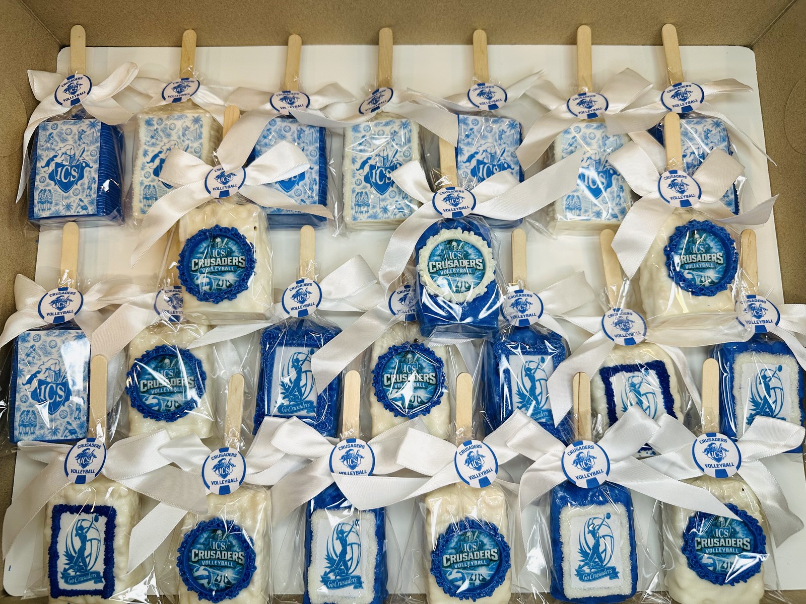 Coordinated blue and white Crusaders volleyball chocolate covered Rice Krispie treat collection with bows, framed logos, and printed designs