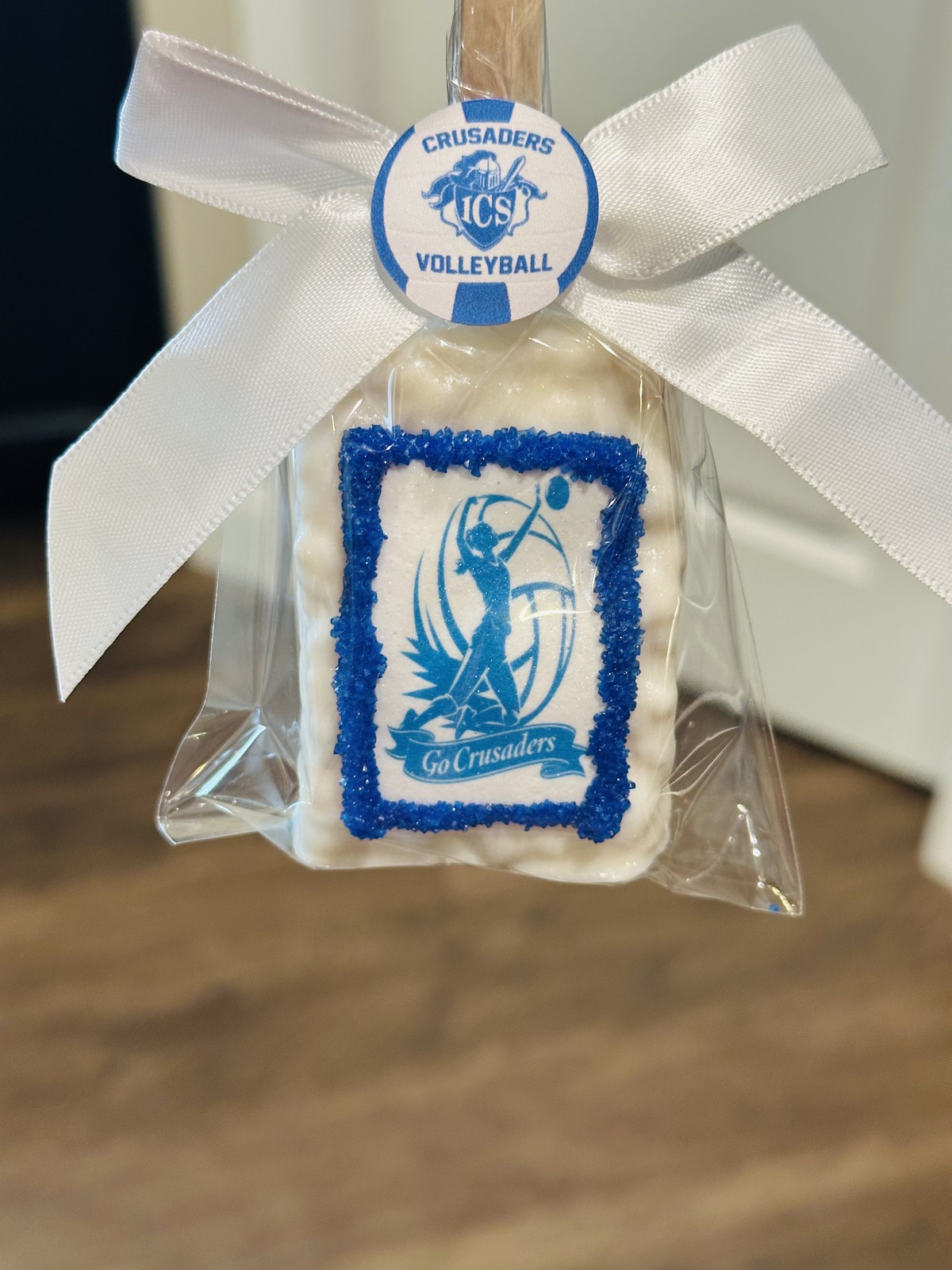 Individually wrapped white Crusaders volleyball chocolate covered Rice Krispie treat with blue printed edible design and white bow