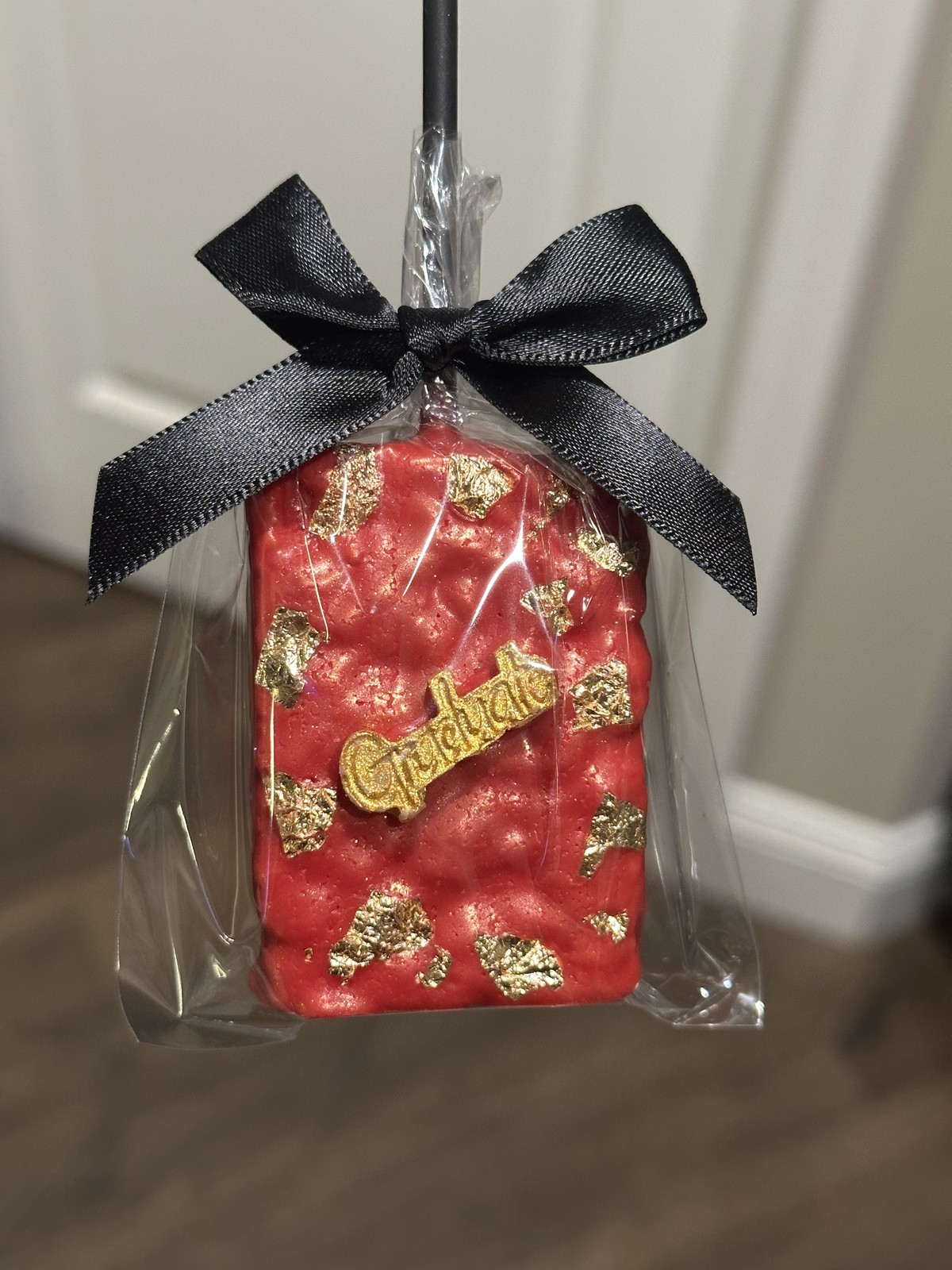 Individually wrapped red and gold chocolate covered Rice Krispie treat with decorative chocolate bubbles and black bow